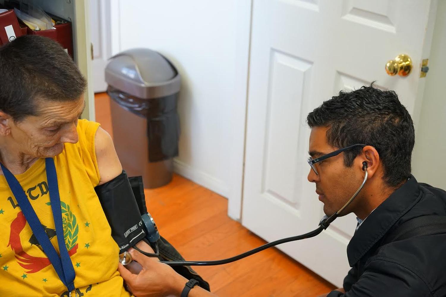 A visiting resident physician checks blood pressure for a patient housed in a Board and Care Facility.  Taken by Dr. Coley King of Venice Family Clinic.