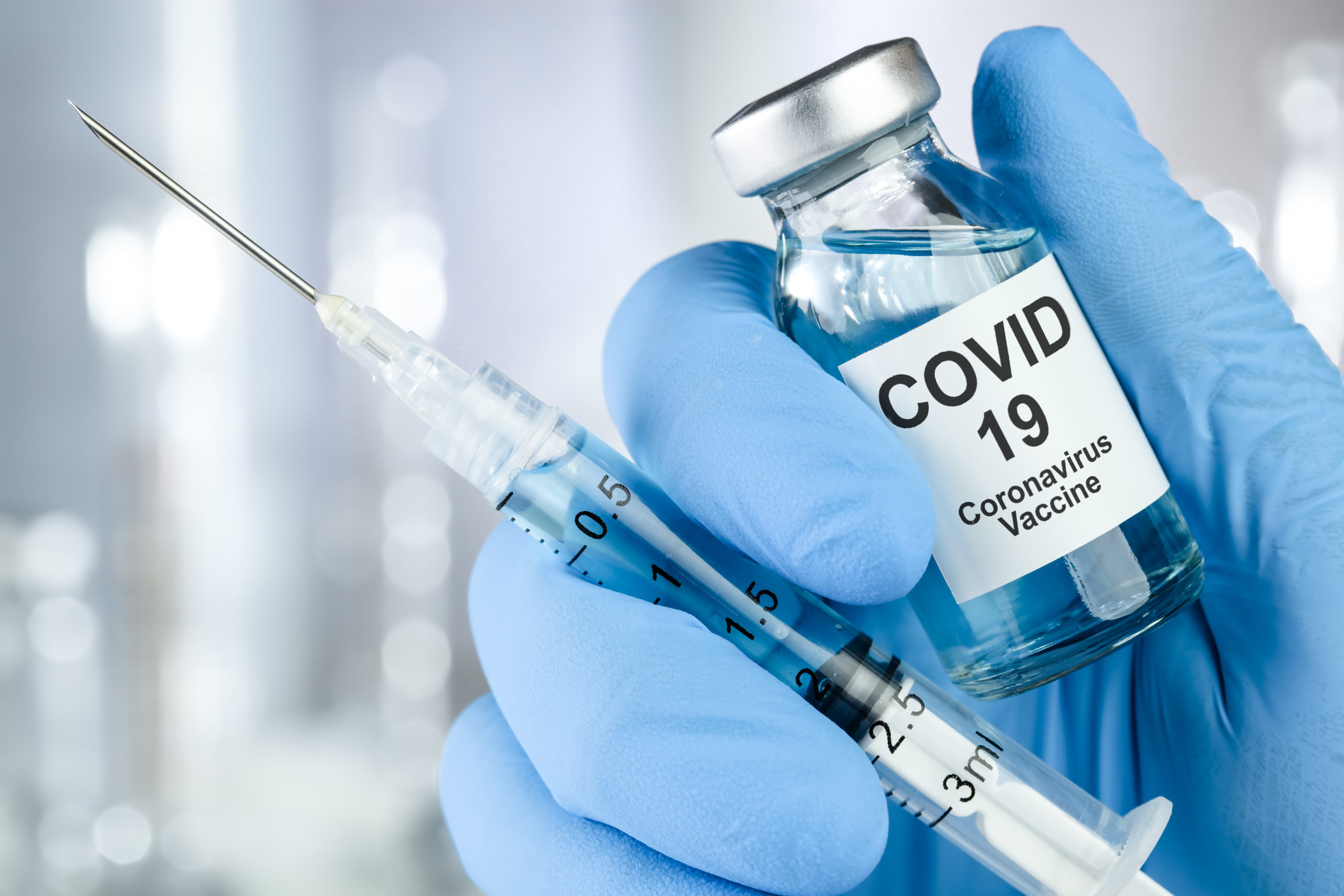 A Gloved Hand Holds A Vial Labeled COVID-19 Coronavirus Vaccine And A Syringe Filled With Liquid, Symbolizing Vaccination Efforts Against The Coronavirus.