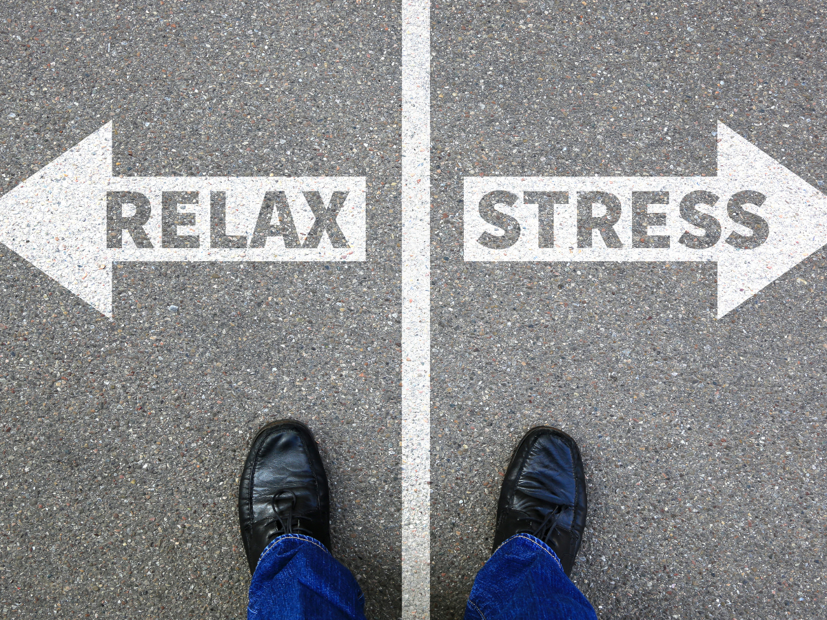 A Person In Black Shoes And Jeans Stands At A Crossroads On Pavement, With Arrows Pointing Left To RELAX And Right To STRESS, Symbolizing A Choice Between Relaxation And Stress.