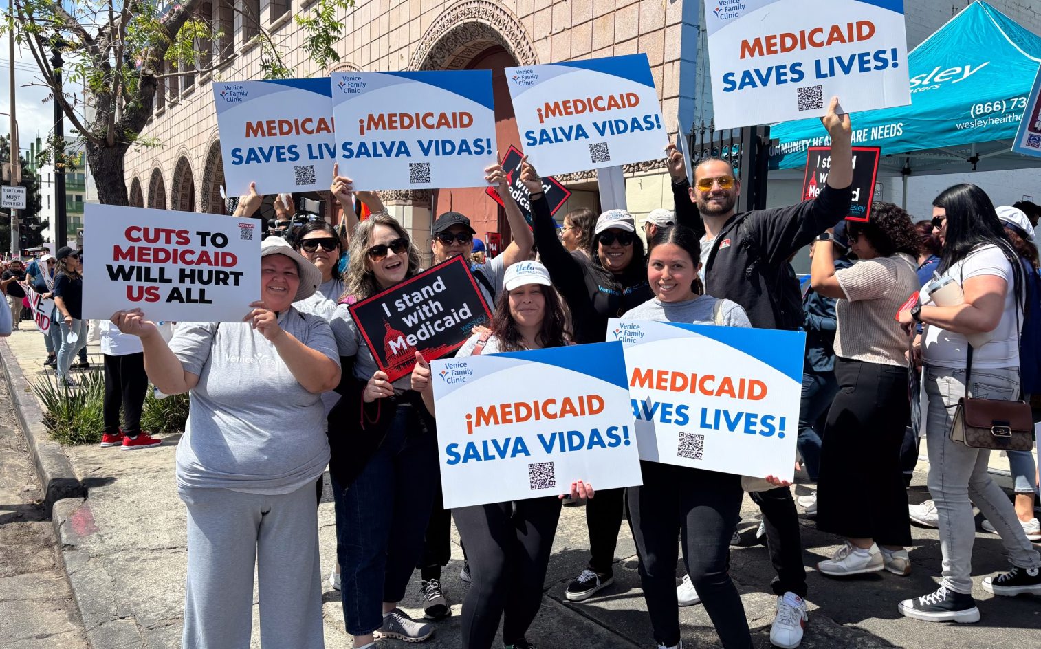 A Group Of People At A Rally Hold Up Signs Supporting Medicaid, With Messages In English And Spanish Such As “Medicaid Saves Lives!” And “¡Medicaid Salva Vidas!” They Are Smiling And Appear Enthusiastic. A Group Of People At A Rally Hold Up Signs Supporting Medicaid, With Messages In English And Spanish Such As “Medicaid Saves Lives!” And “¡Medicaid Salva Vidas!” They Are Smiling And Appear Enthusiastic.