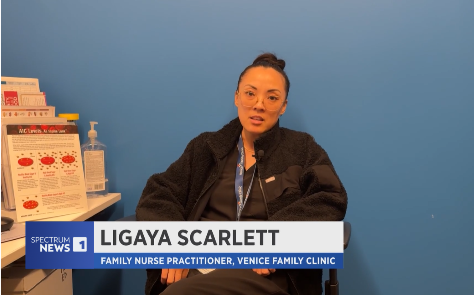 A woman wearing glasses and a black jacket sits in a clinic office with blue walls, speaking in an interview. Text on screen reads: Ligaya Scarlett, Family Nurse Practitioner, Venice Family Clinic and Spectrum News 1. A woman wearing glasses and a black jacket sits in a clinic office with blue walls, speaking in an interview. Text on screen reads: Ligaya Scarlett, Family Nurse Practitioner, Venice Family Clinic and Spectrum News 1.