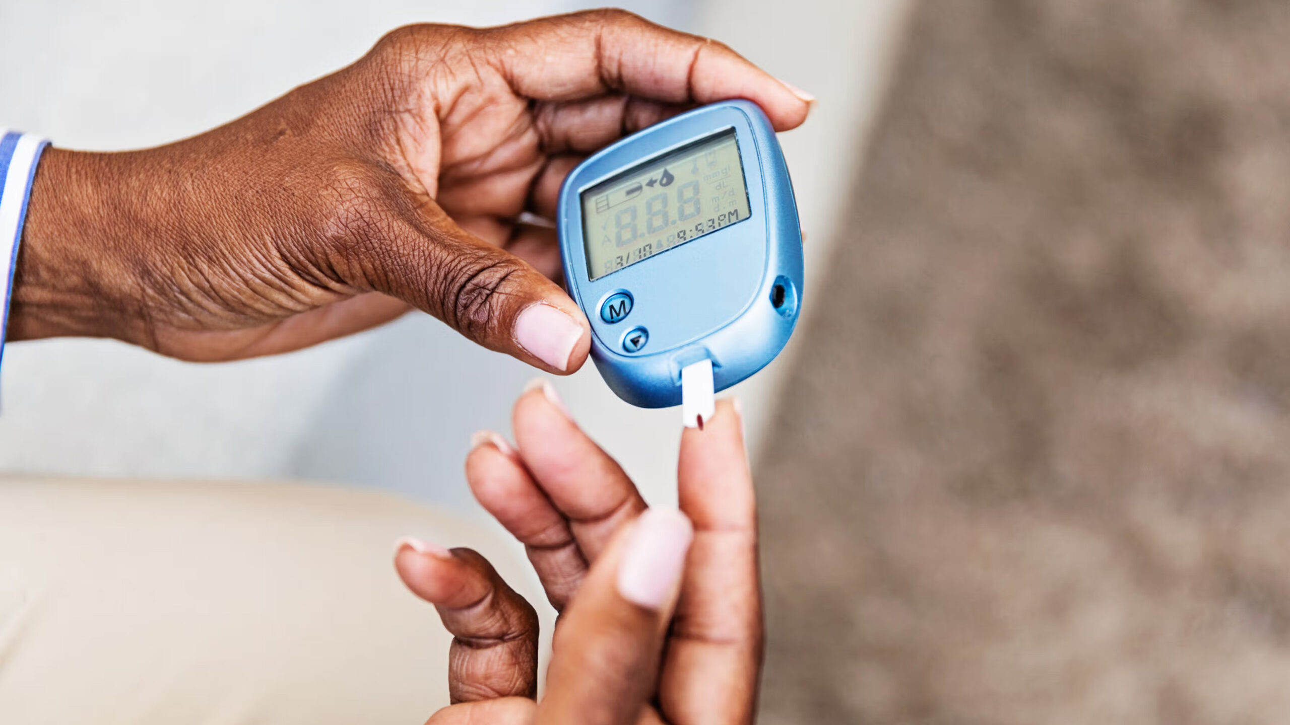 A Person Holds A Blue Blood Glucose Meter In One Hand While Using The Other Hand To Test Their Blood Sugar Level With A Test Strip.