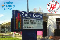 An Outdoor Sign For Zela Davis Elementary School Displays Winter Break Dates. Logos For Venice Family Clinic And Hawthorne School District Are Visible On The Image. The School Building And A Fence Are In The Background.