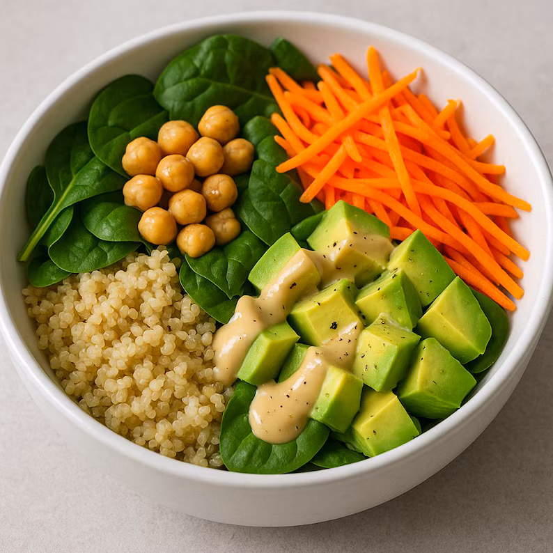A White Bowl Filled With Spinach Leaves, Chickpeas, Shredded Carrots, Cubed Avocado With Dressing, And Cooked Quinoa, Arranged In Separate Sections.