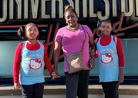 A Woman Standing Between Two Girls Wearing Matching Hello Kitty Tank Tops In Front Of A Universal Studios Sign.