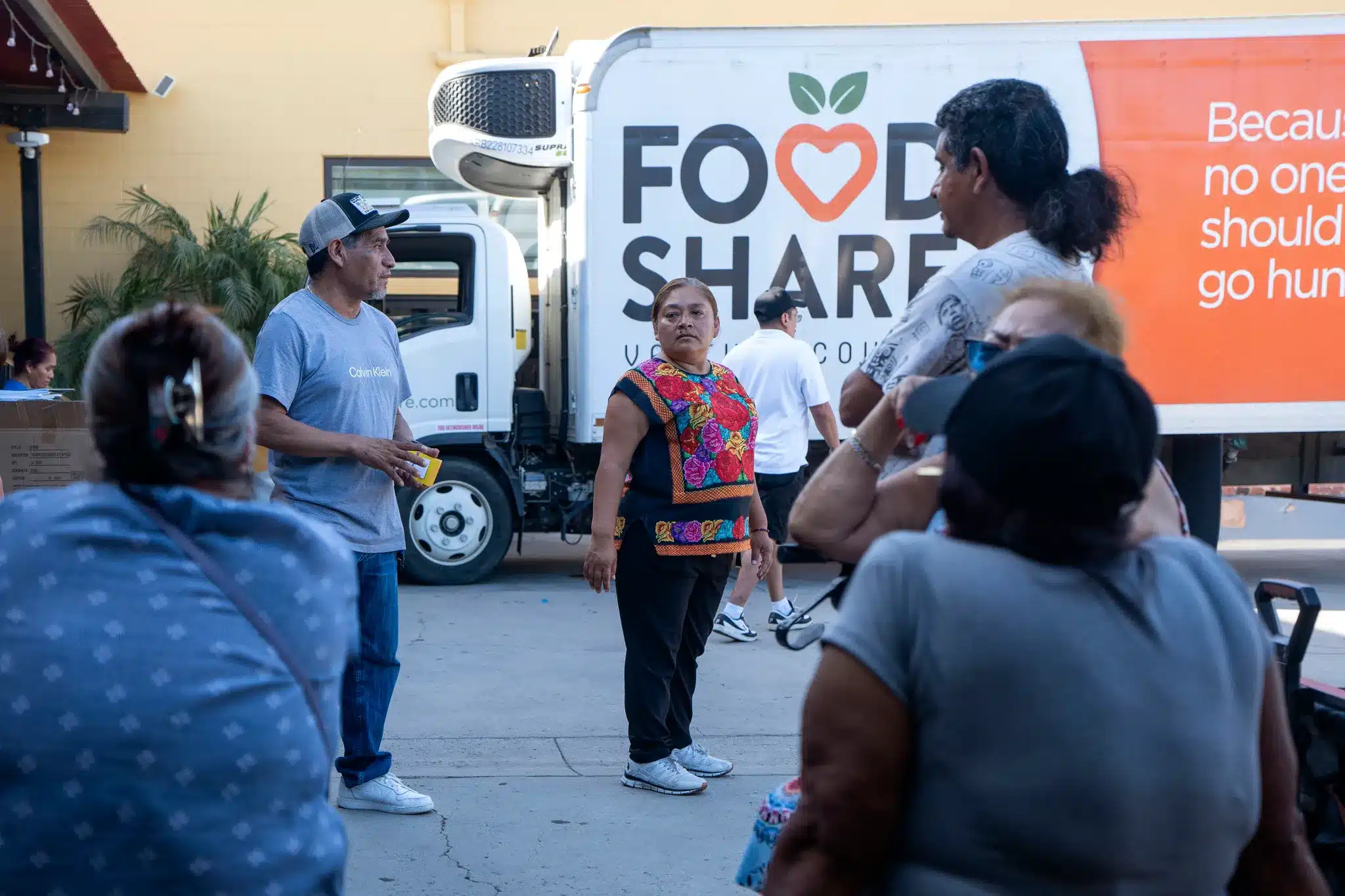 People Stand In Line In Front Of A Food Share Truck. People Stand In Line In Front Of A Food Share Truck.